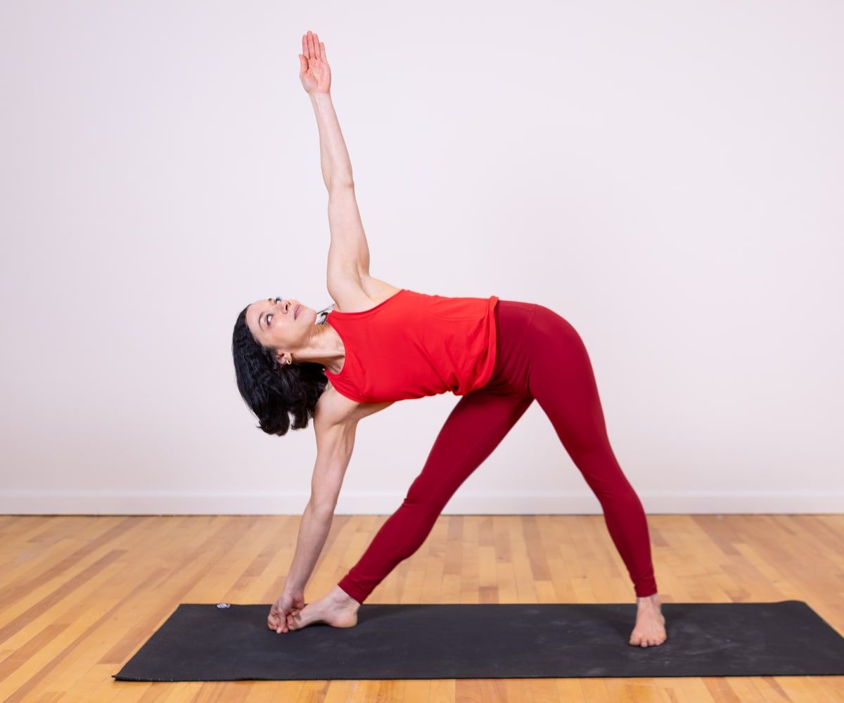 Chloe Foster in a standing yoga pose, one leg extended, in a red top.