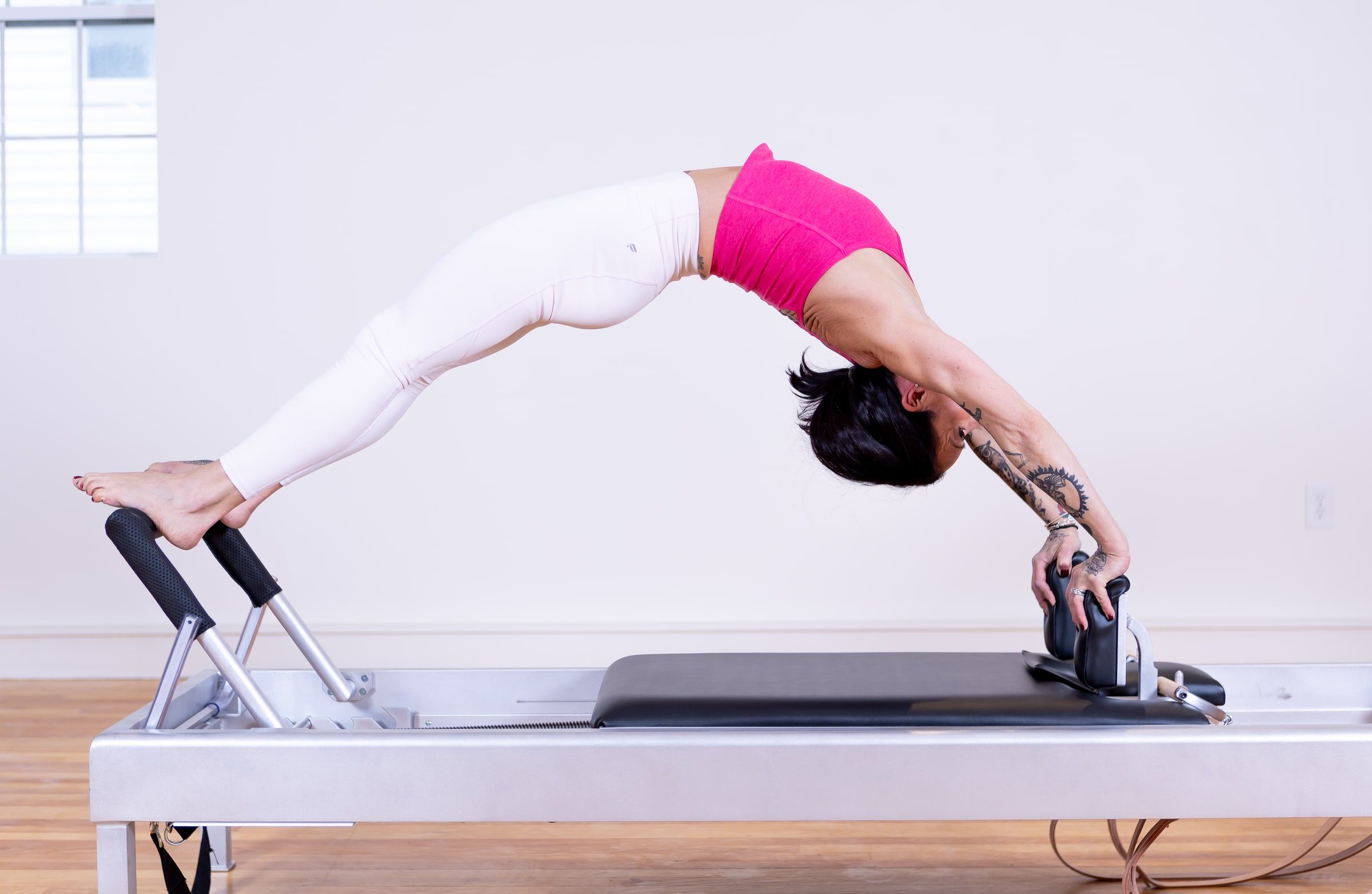 A student arched into a high bridge over the Pilates reformer, hands and feet on the carriage.