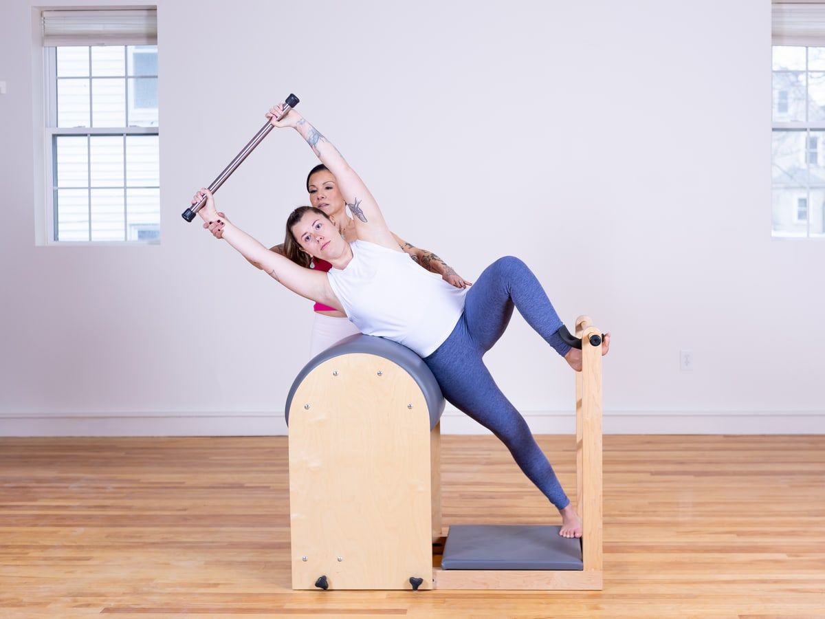 An instructor guiding a client through a stretch on the Pilates Cadillac.